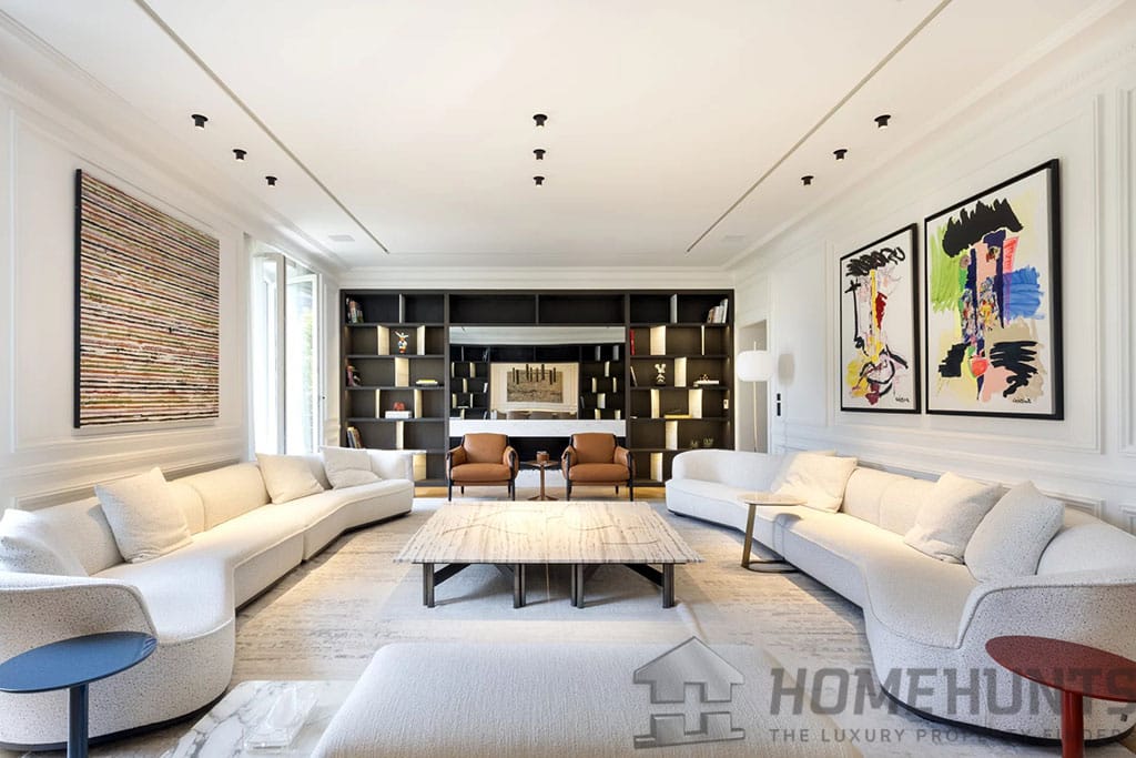 Looking to Buy in Paris? Discover 5 Incredible Luxury Apartments for Sale 3 Image of a modern living room in a Paris apartment with curved white sofas, abstract artwork, a marble coffee table, and a large built-in bookshelf.