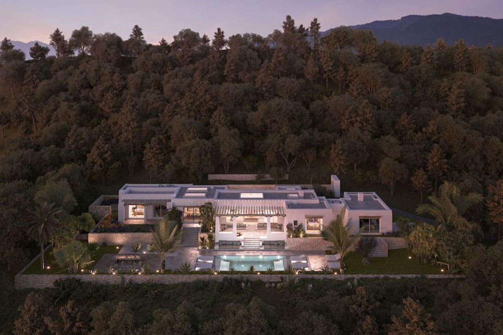 Find Your Dream Villa in Ibiza’s Most Prestigious Locations 6 Image of a modern hillside villa in Ibiza surrounded by dense trees, featuring a central pool, landscaped gardens, and warm evening lighting.