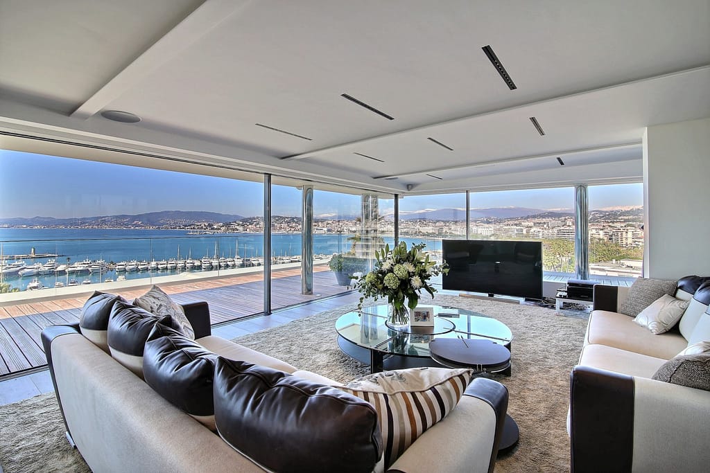 Image of a contemporary living room with comfortable seating, large windows, and a scenic view extending over Cannes and the sea.