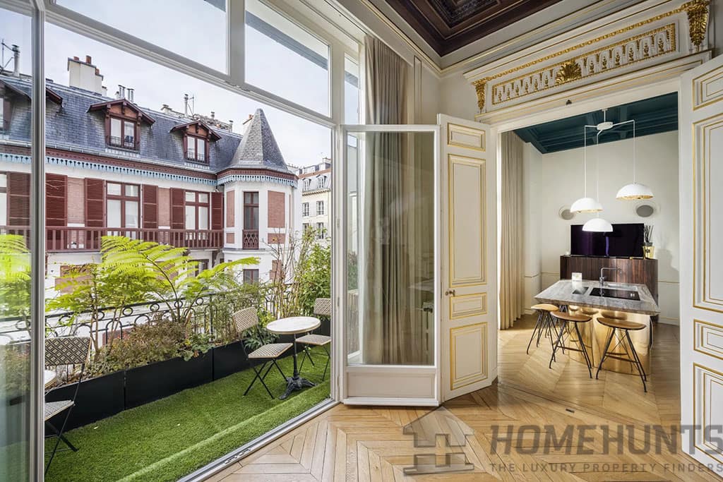 Looking to Buy in Paris? Discover 5 Incredible Luxury Apartments for Sale 2 Image of a stylish apartment with a small balcony featuring outdoor seating, gold-trimmed doors, and an elegant kitchen with pendant lighting.