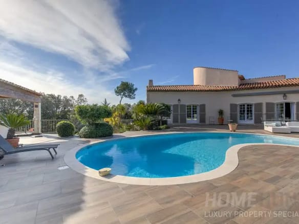 Image of a modern villa with a curved swimming pool, sun loungers, and landscaped greenery under a clear blue sky illustrating Buying Property in France After Brexit