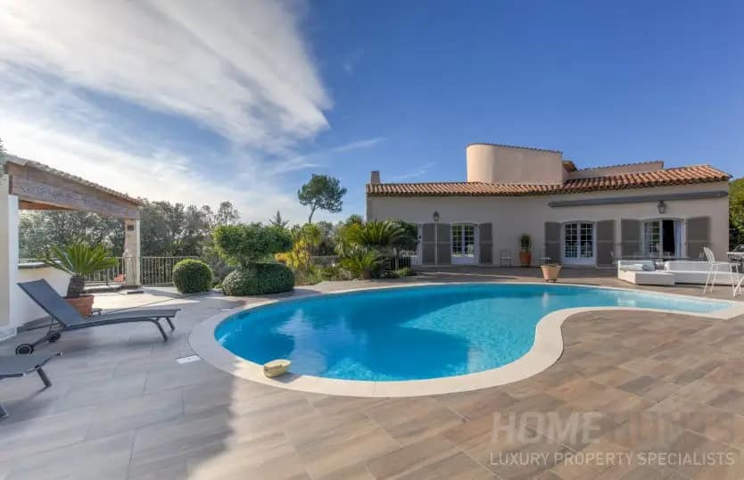 Image of a modern villa with a curved swimming pool, sun loungers, and landscaped greenery under a clear blue sky illustrating Buying Property in France After Brexit
