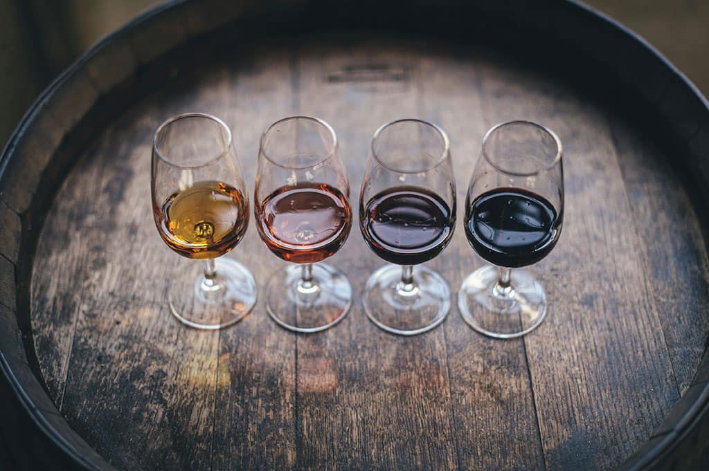 Insider Tips for First-Time Vineyard Buyers 5 Image of four glasses of win lined up on a wooden barrel ready for wine tasting in a french vineyard.